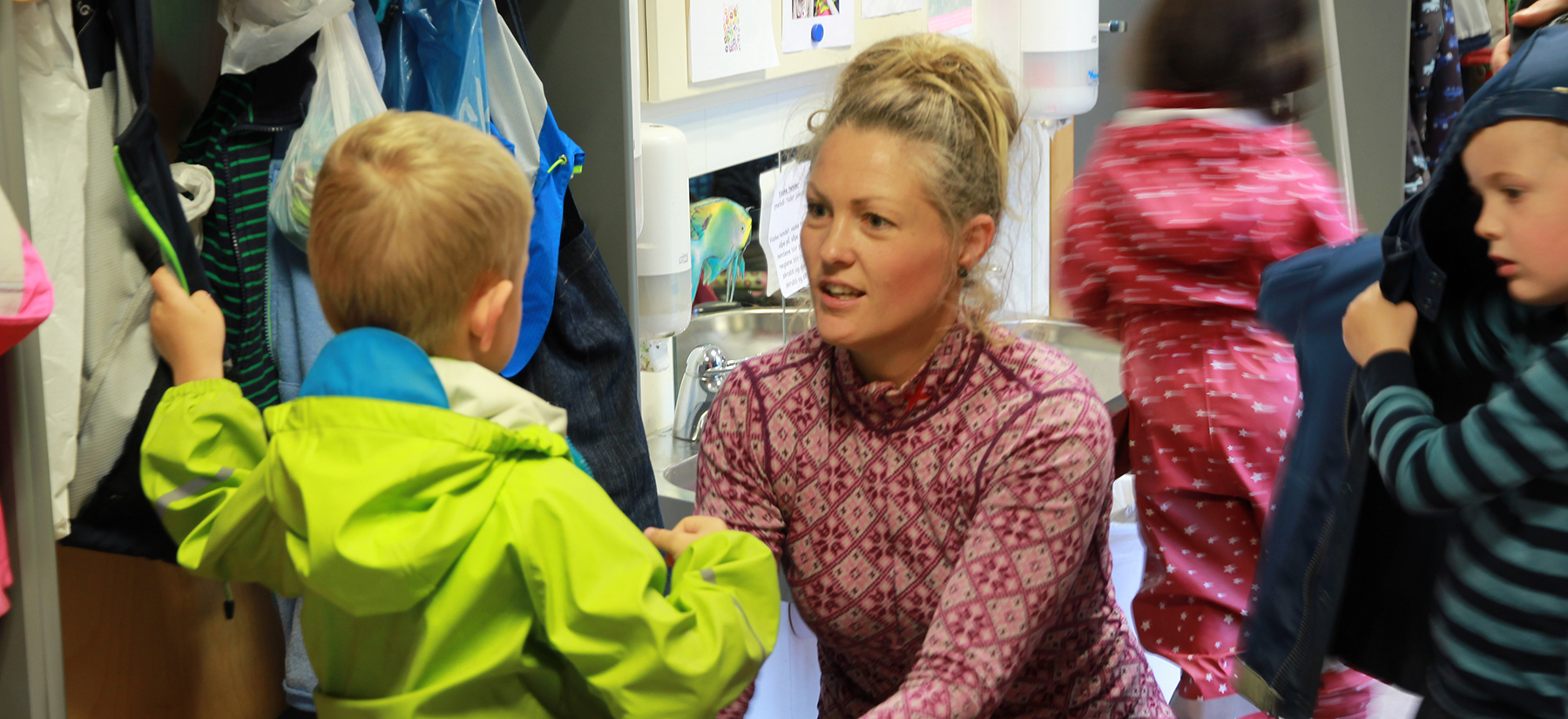 Barnehagelærer snakker med to gutter i garderoben