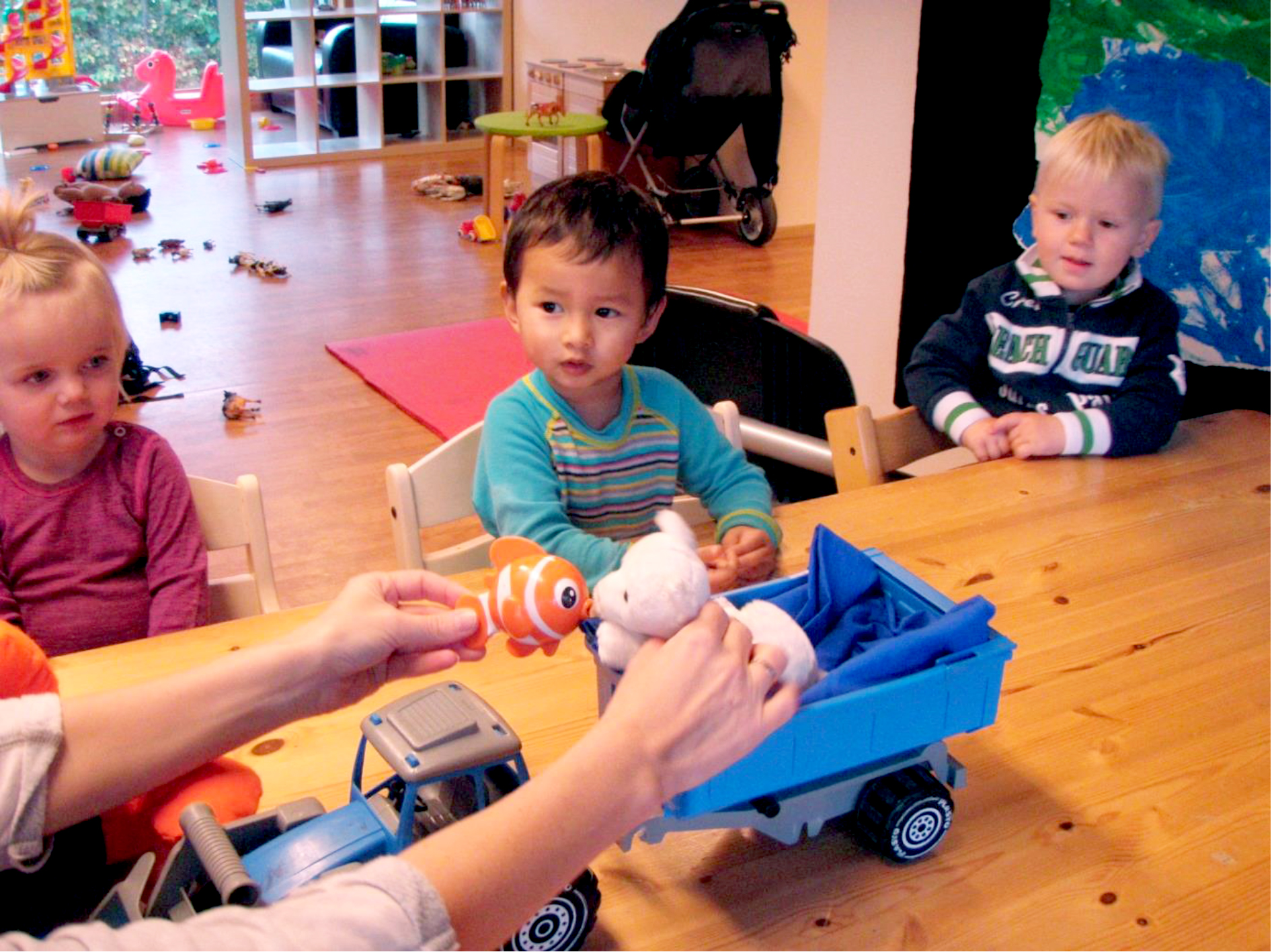 Tre barn sitter ved et bord i en barnehage