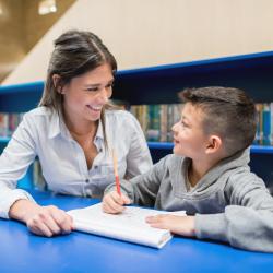 Pedagog og elev sitter ved et bord og ser på hverandre
