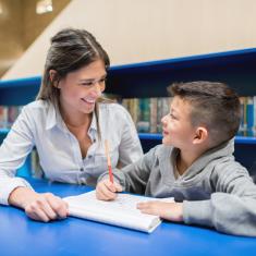 Pedagog og elev sitter ved et bord og ser på hverandre